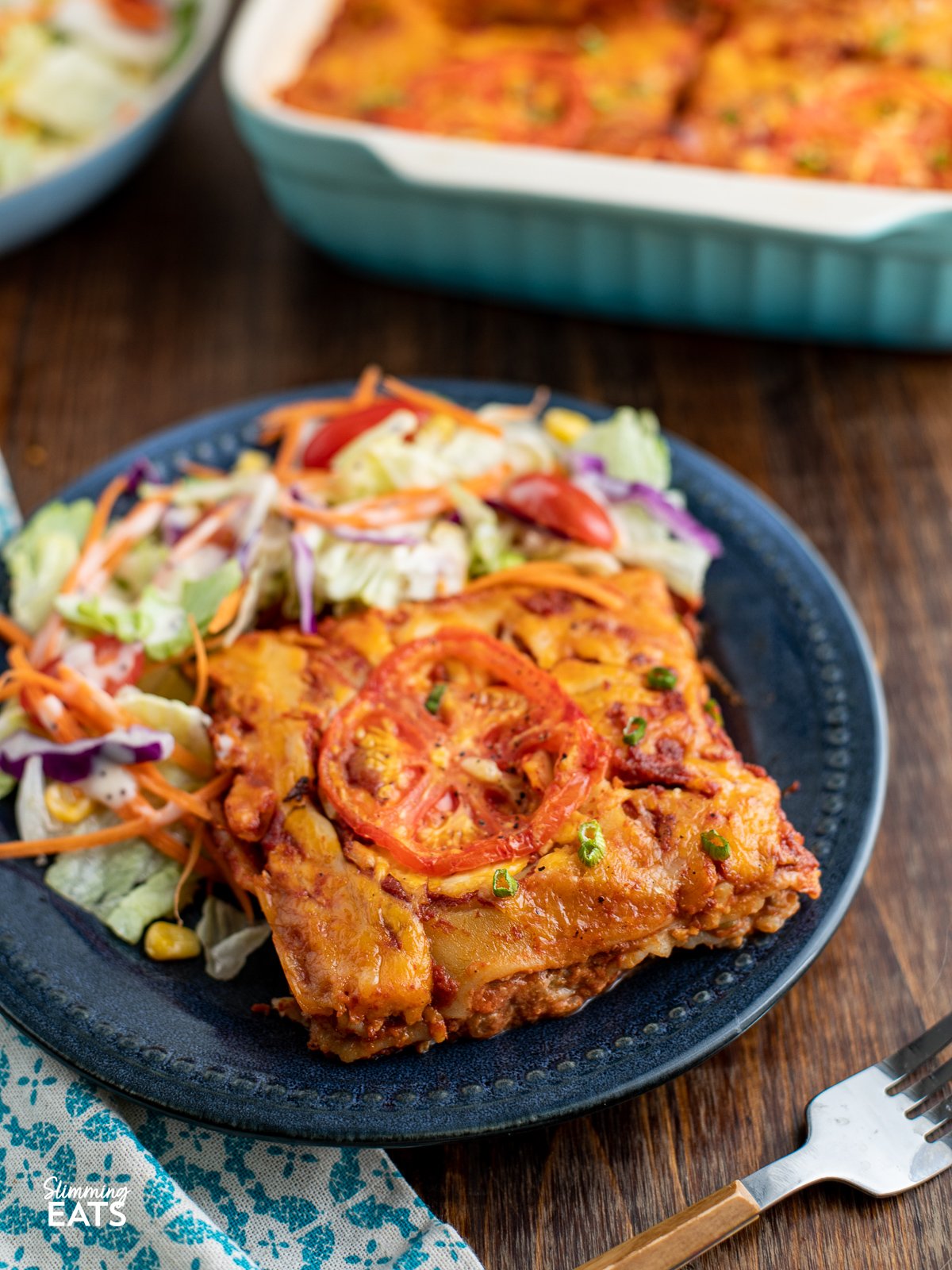serving of Spicy Mexican Chicken Lasagne on a dark blue plate with salad