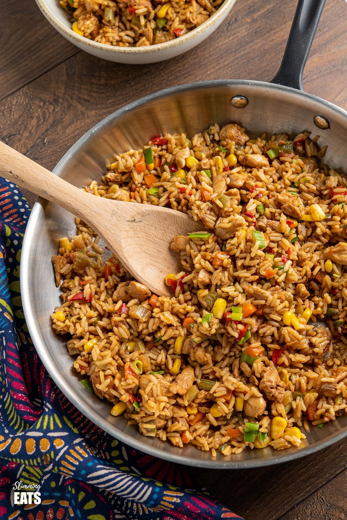 savoury rice in stainless steel frying pan with black handle, bowl of rice in background