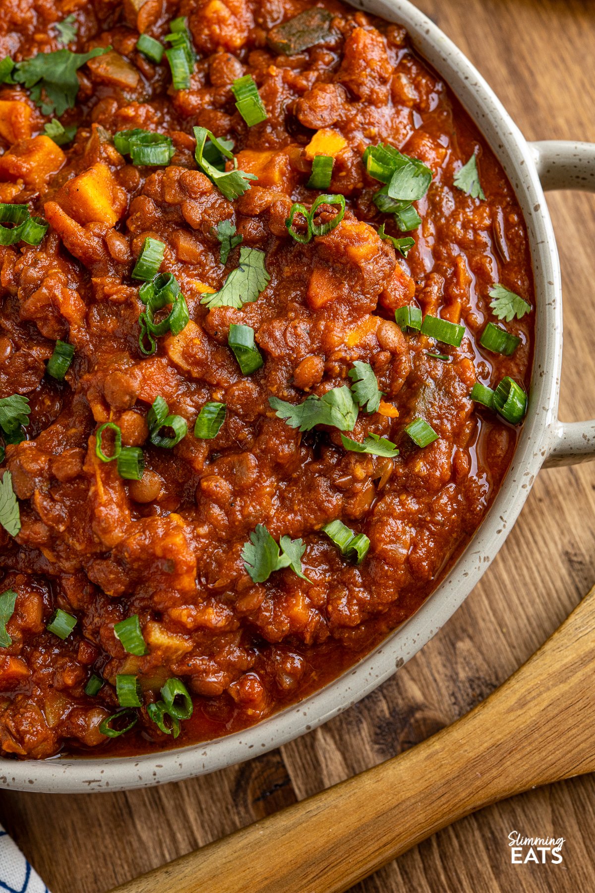 Enjoy a comforting and filling bowl of Sweet Potato, Vegetable and Lentil Chilli with some of your favourite toppings. Vegetarian and Slimming Friendly close up of Sweet Potato, Vegetable and Lentil Chilli in a brown grey double handled dish
