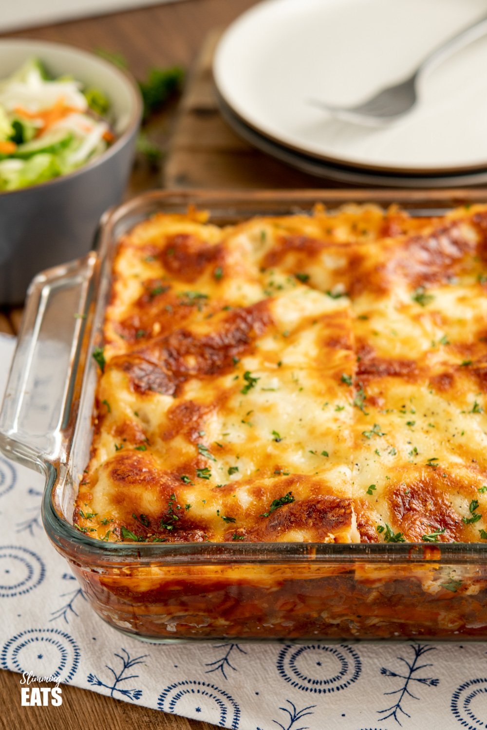 sliced lasagne in pyrex dish with plates and salad bowl in background