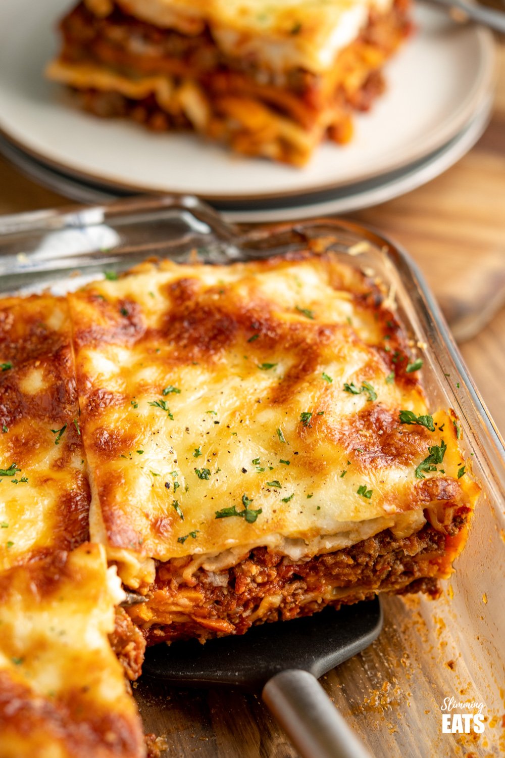 The BEST Low Syn Beef Lasagne - amazingly rich beef sauce in between layers of pasta and sweet potato, all finished off with a delicious healthier bechamel white sauce and melted cheese. Gluten Free, Slimming World and Weight Watchers friendly. slice of beef asagne on spatula in pyrex dish