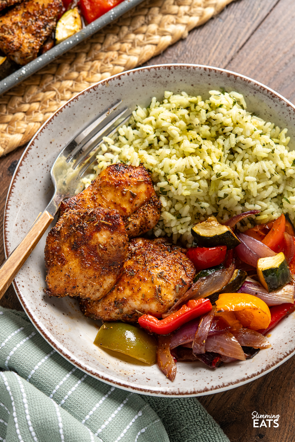 close up of black pepper chicken, served alongside balsamic roasted vegetables and herby seasoned rice in a bowl with wooden handled fork place in left hand side of bowl 