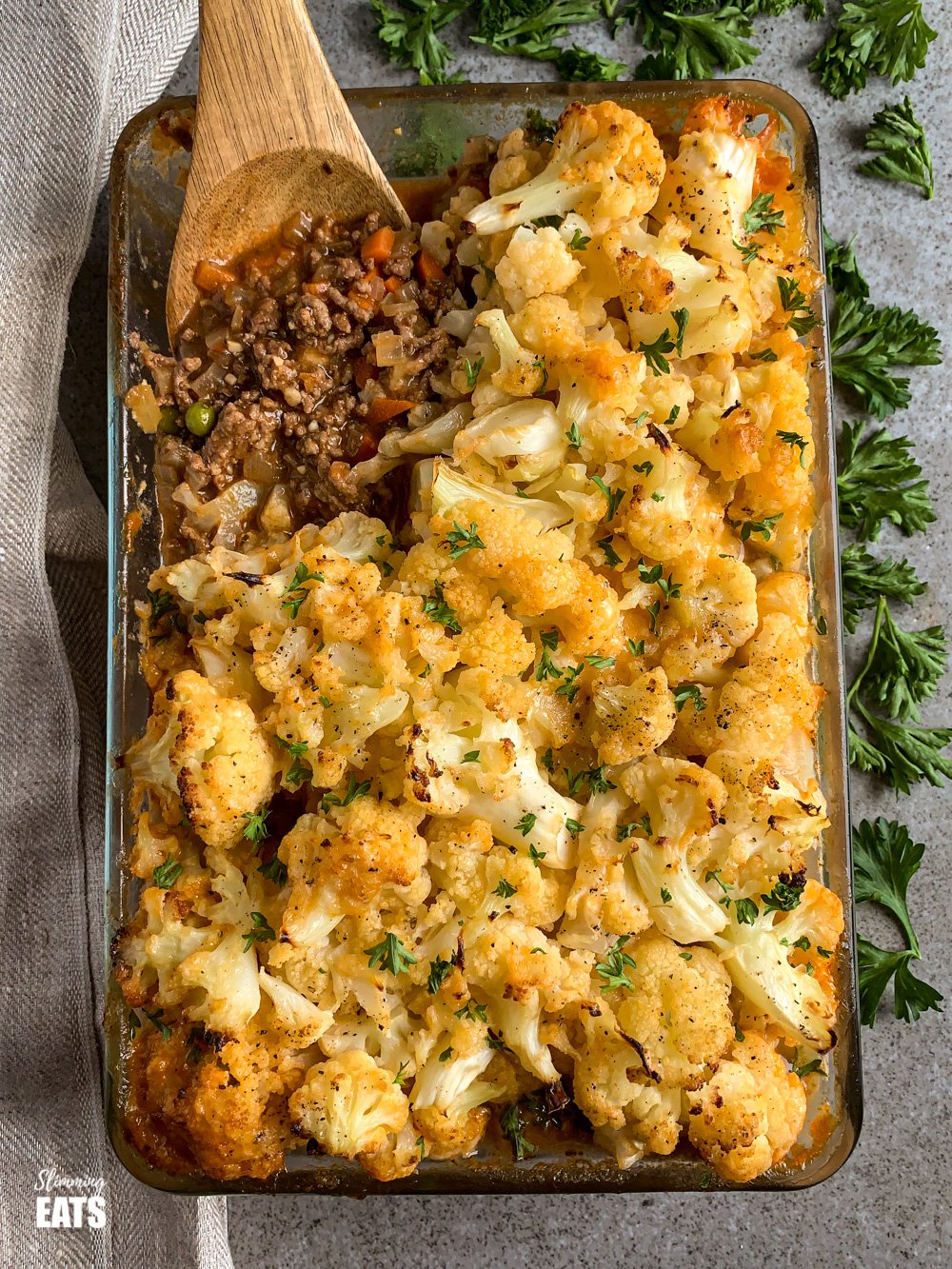 wooden spoon scooping Cheesy Cauliflower Topped Pie from a glass oven dish