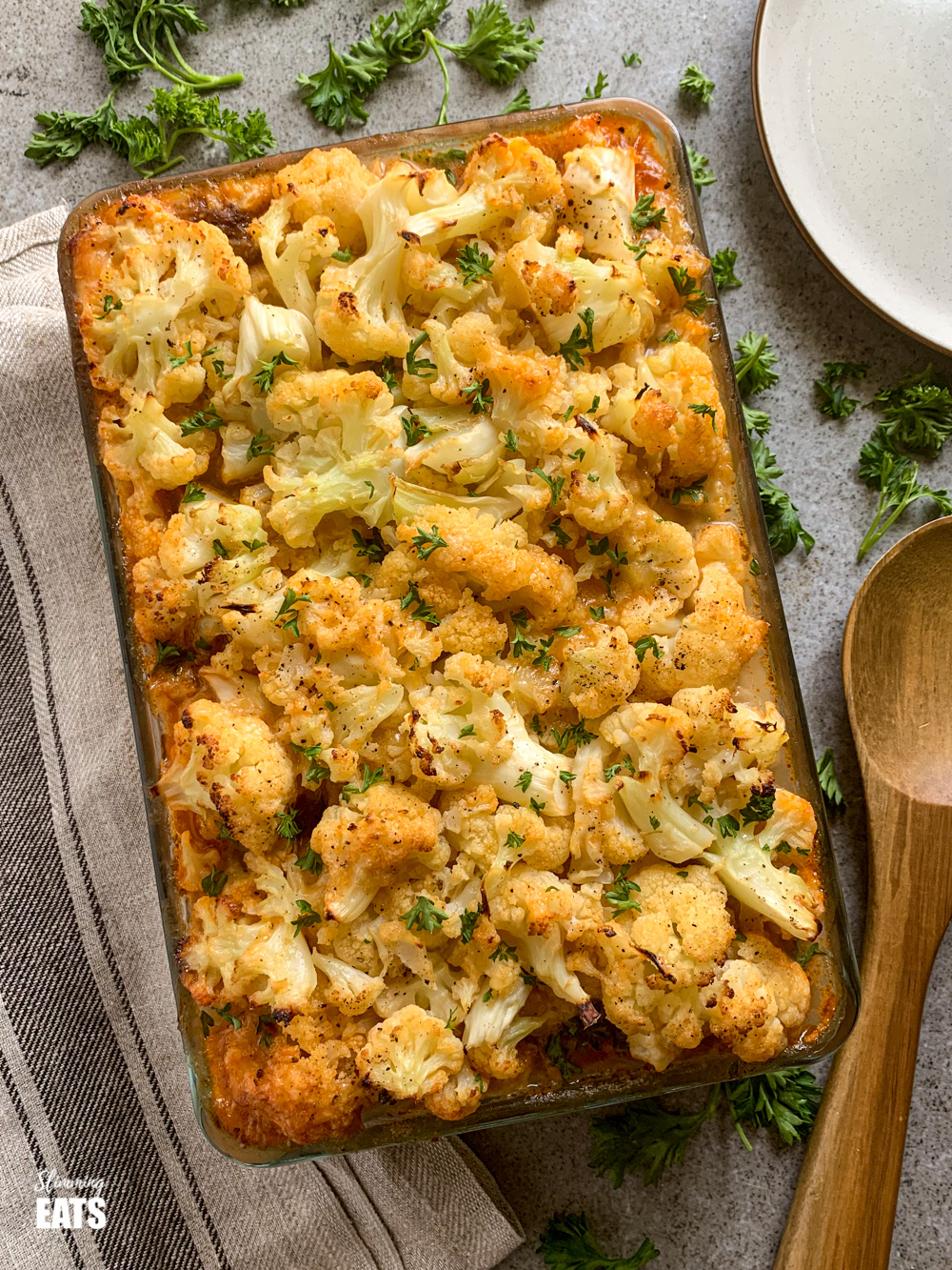 Cheesy Cauliflower Topped Pie in a glass oven dish on board with wooden spoon to the right