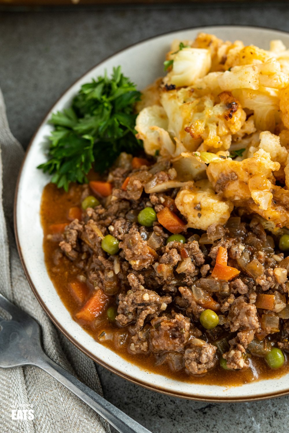 Cheesy Cauliflower Topped Pie - all the goodness of a traditional cottage pie but topped with delicious tender cheesy cauliflower florets. Gluten free, Slimming Eats and Weight Watchers friendly close up of cheesy cauliflower topped pie dishes up in white bowl with fresh parsley.