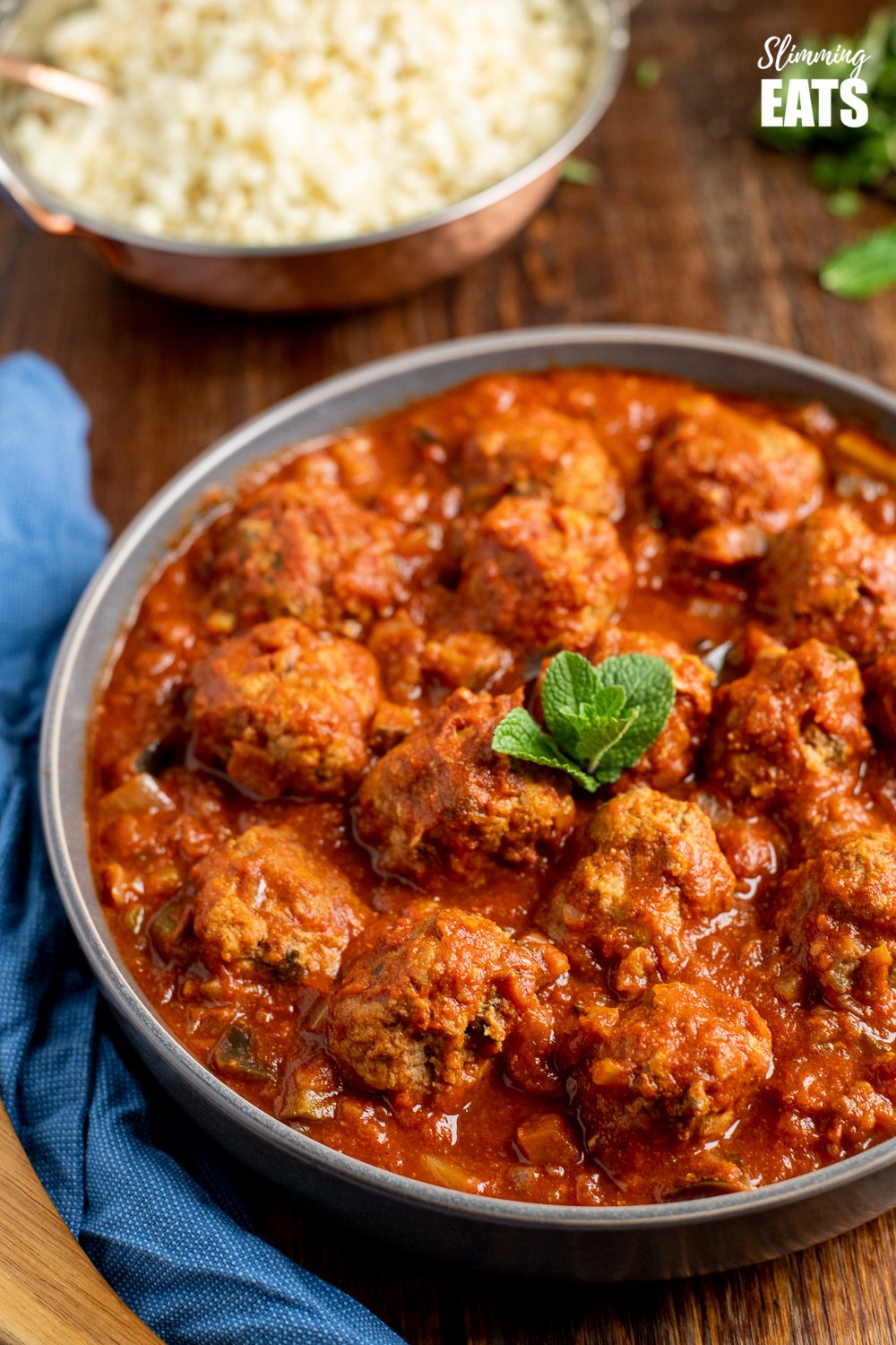 lamb and mint meatballs in a sweet and spicy sauce in a grey bowl on wooden board with bowl of cauliflower rice