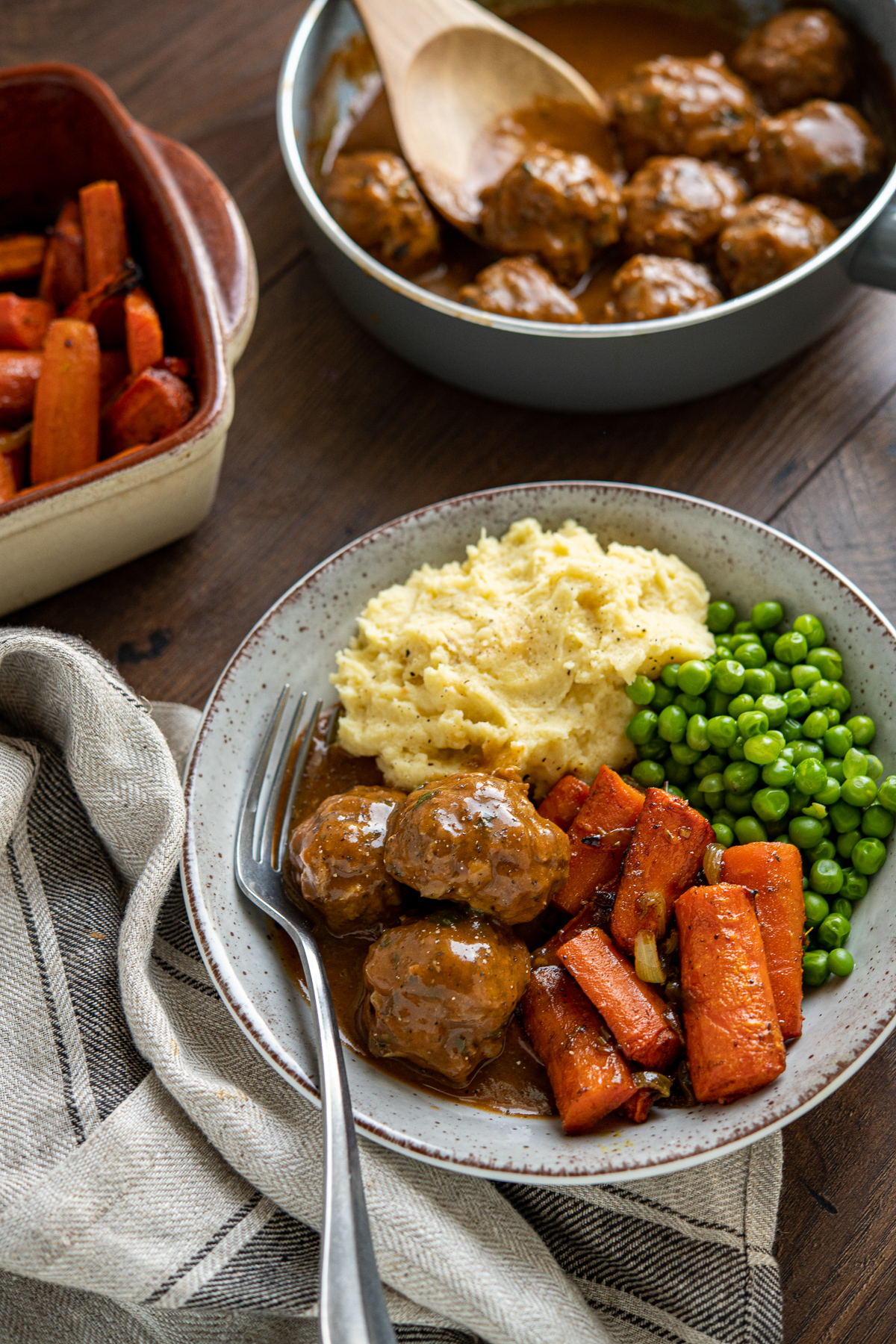 Lamb Meatballs with Mint Gravy in a grey and brown bowl with carrots, onion, peas and mashed potatoes with fork place in the bowl on the left