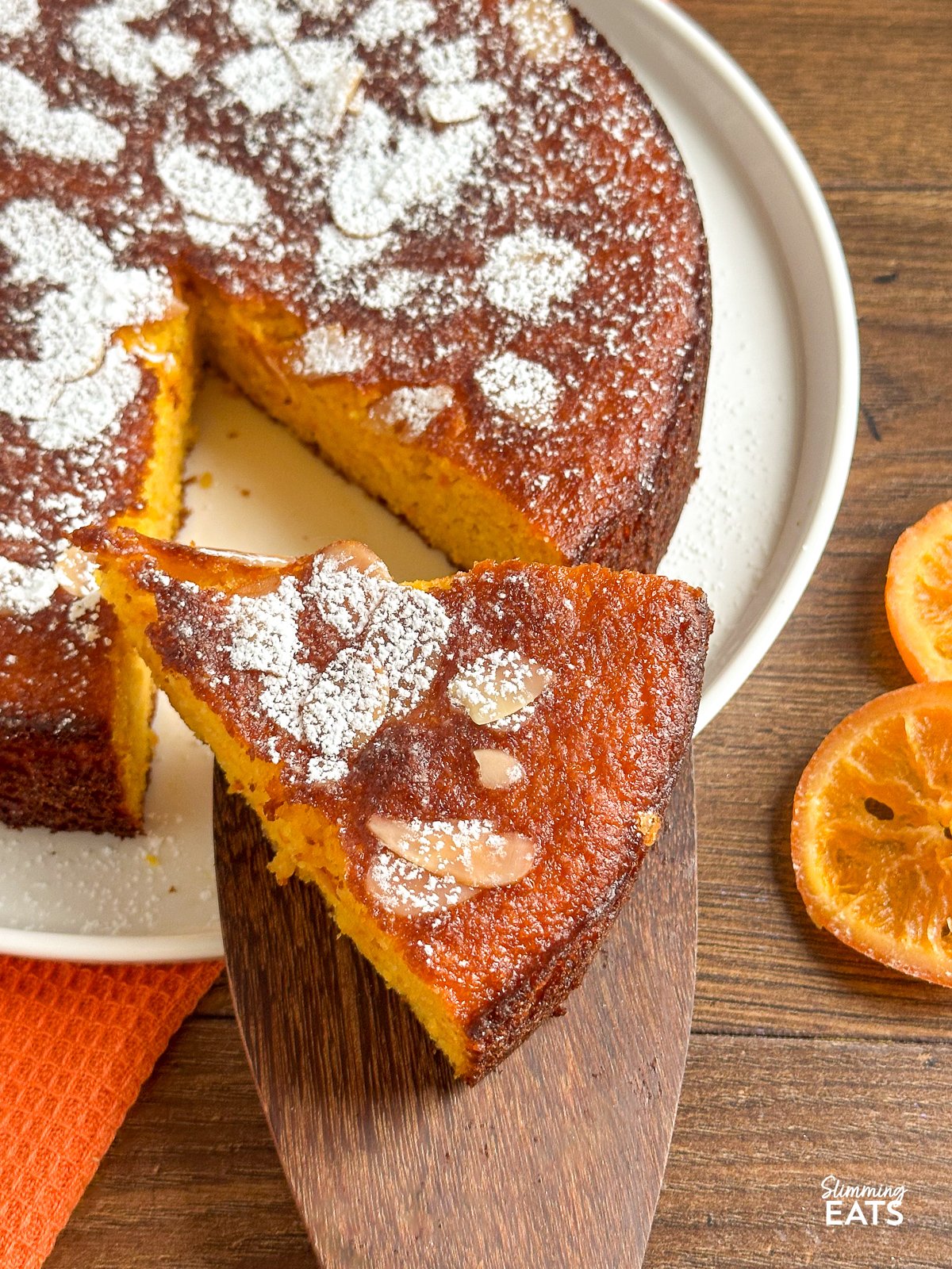 This Flourless Orange Almond Cake is a delightful fusion of almond richness and the zingy essence of oranges. With just a handful of simple ingredients, this grain-free and gluten-free creation yields a moist crumb with a subtle sweetness, perfectly complemented by a burst of vibrant orange flavour. Clementine Orange Almond Cake slice on a wooden spatula