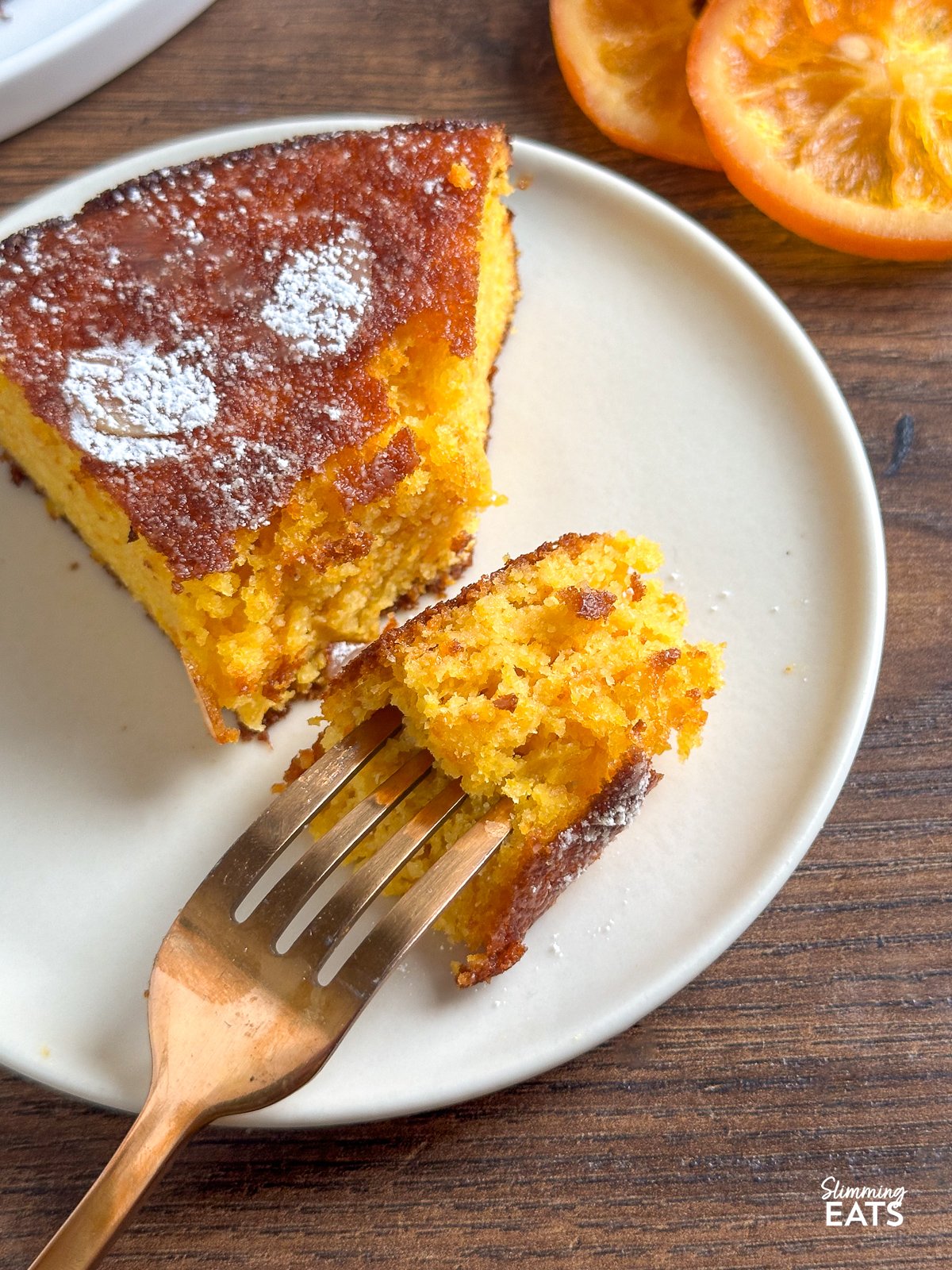 This Flourless Orange Almond Cake is a delightful fusion of almond richness and the zingy essence of oranges. With just a handful of simple ingredients, this grain-free and gluten-free creation yields a moist crumb with a subtle sweetness, perfectly complemented by a burst of vibrant orange flavour. fork in a piece of Clementine Orange Almond Cake on a plate
