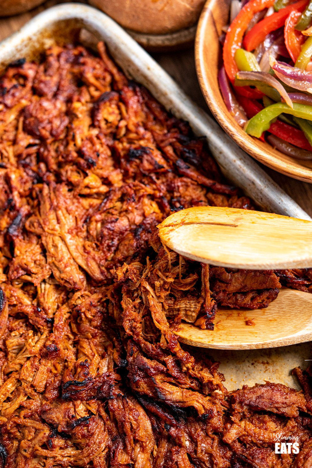 slow cooker pulled pork on baking tray with wooden tonges and bowl of peppers and onion