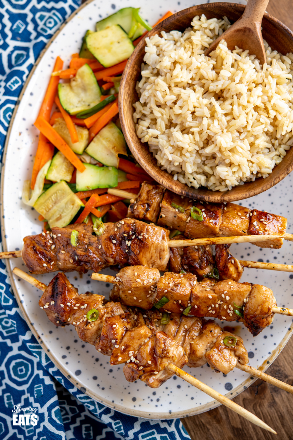 Yakitori Chicken Skewers on speckled plate with a bamboo bowl of brown rice and side fo sesame vegetables