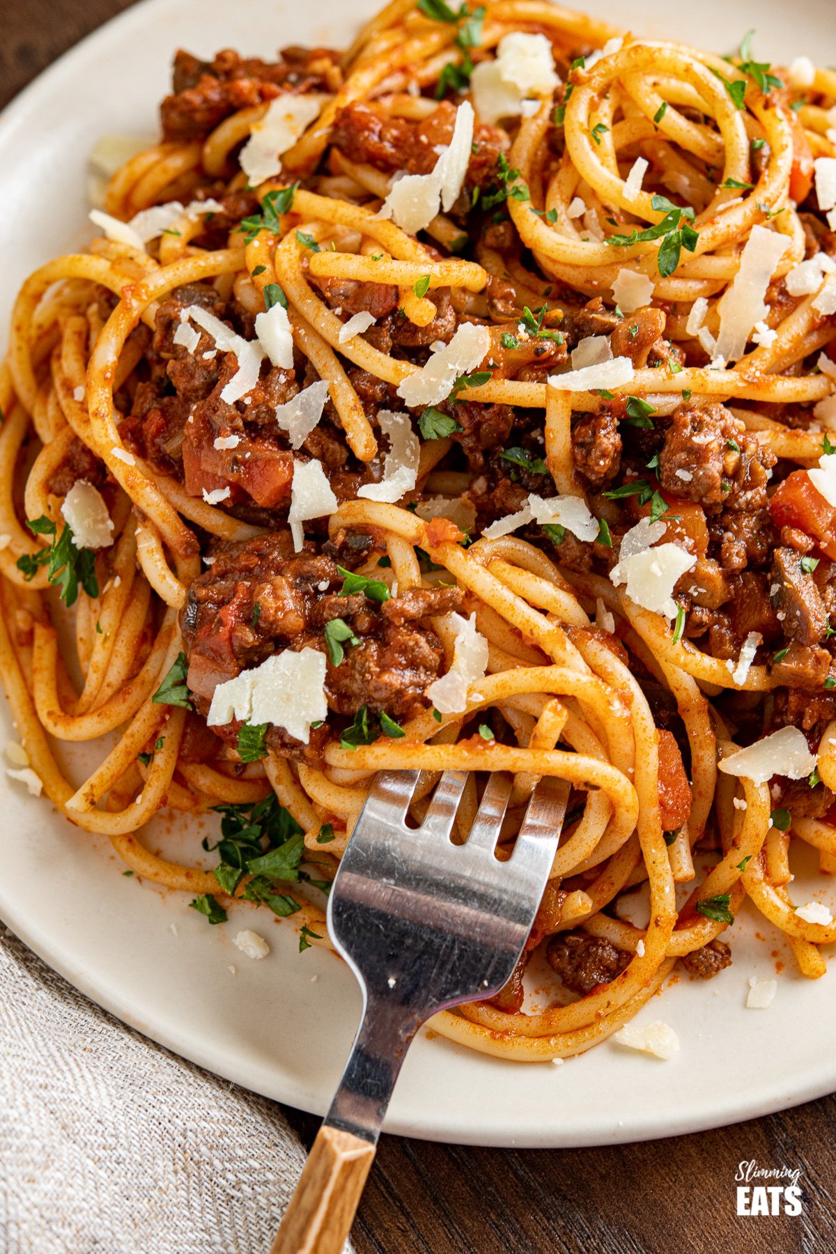 close up spaghetti bolognese on plate with fork and shavings of parmesan on top