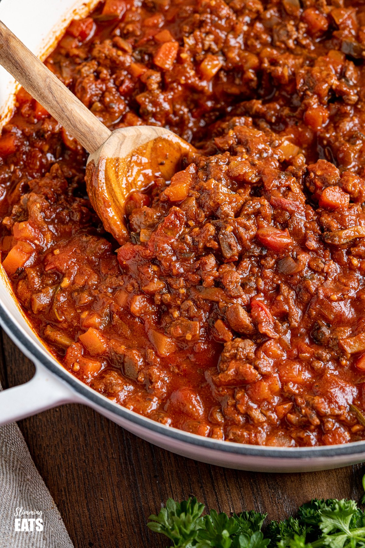 close up of bolognese meat sauce in white cast iron pan with olive wood spoon