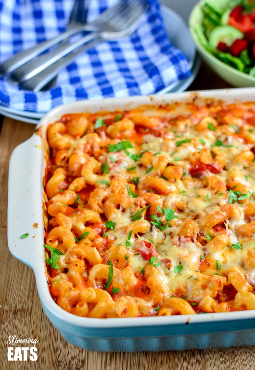 chicken bacon and tomato pasta bake in a blue oven proof dish with plate and napkins in background