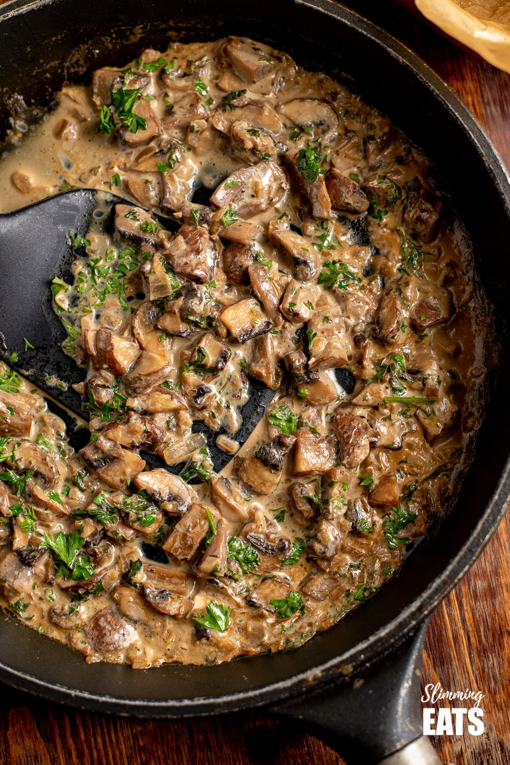 close up of creamy garlic mushrooms in black frying pan with spatula