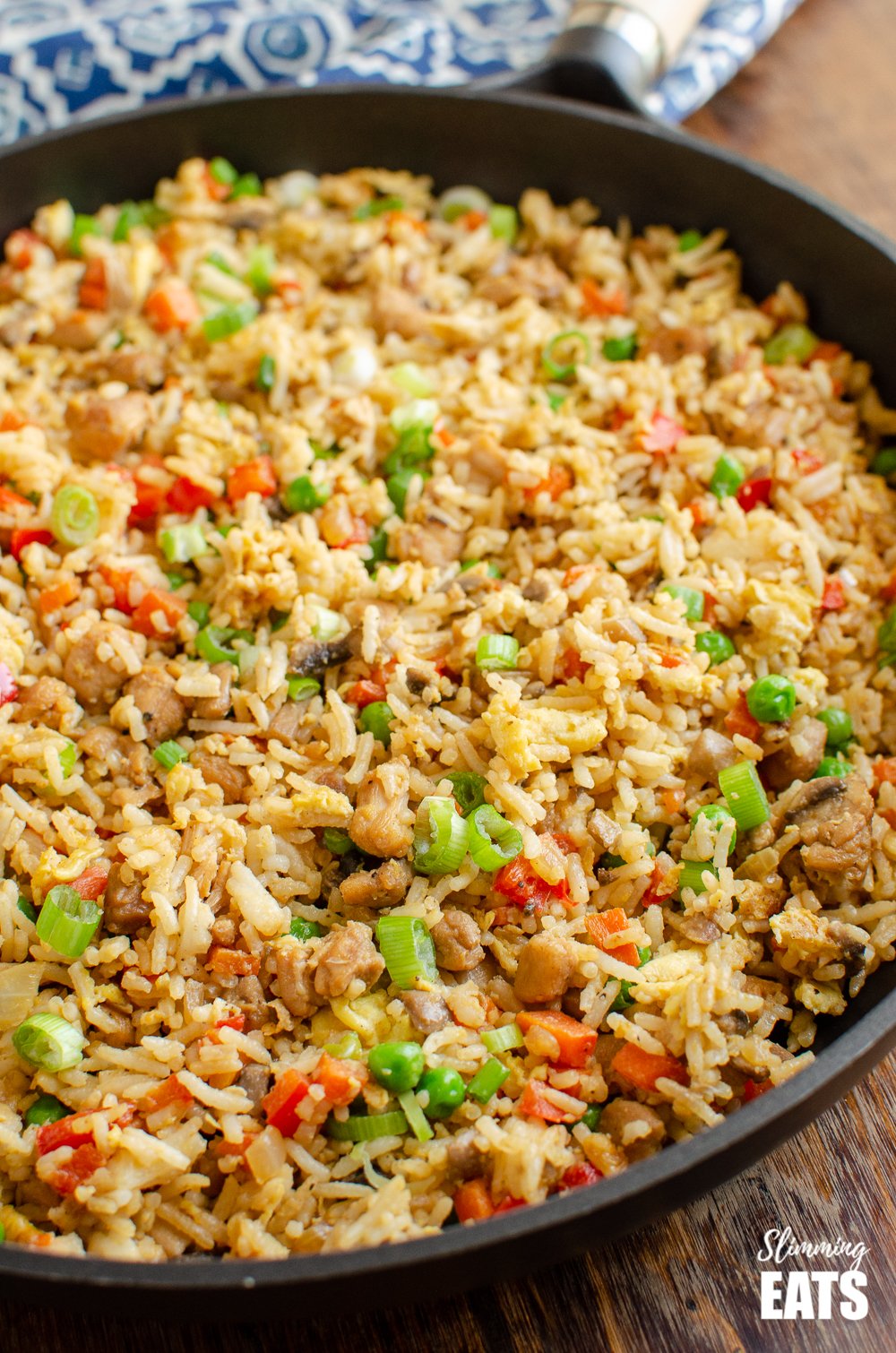 chicken fried rice in a frying pan on a blue pattern placemat and wooden board