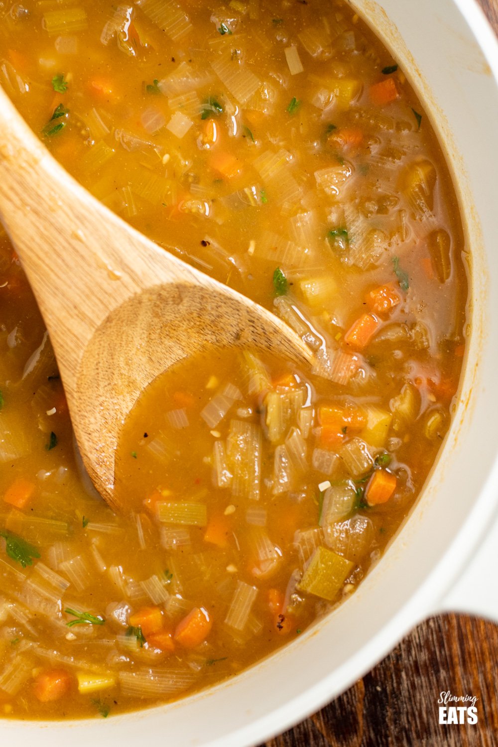 close up of hearty vegetable soup in pan with wooden spoon