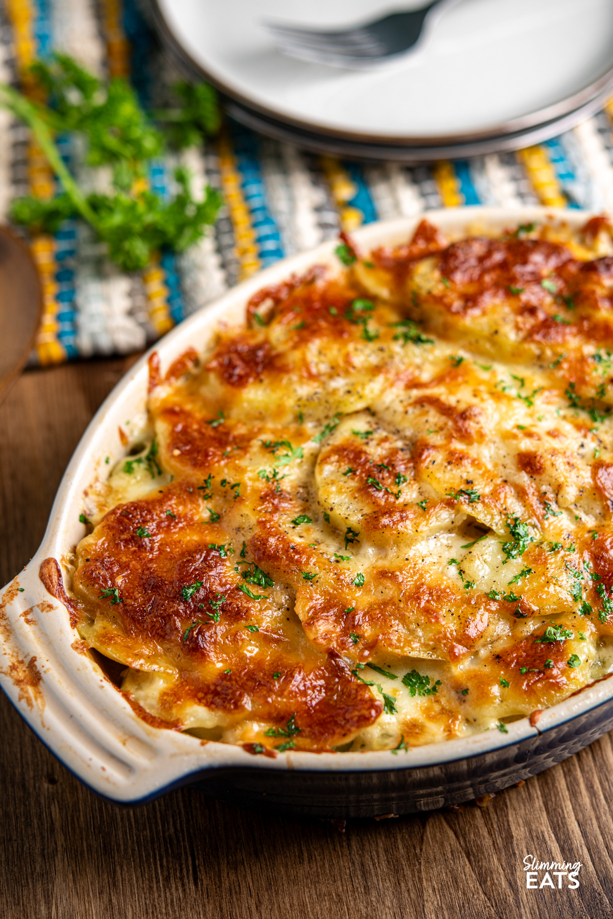 cheesy leek and potato bake in a le Creuset oval dish on wooden board with plates and fork