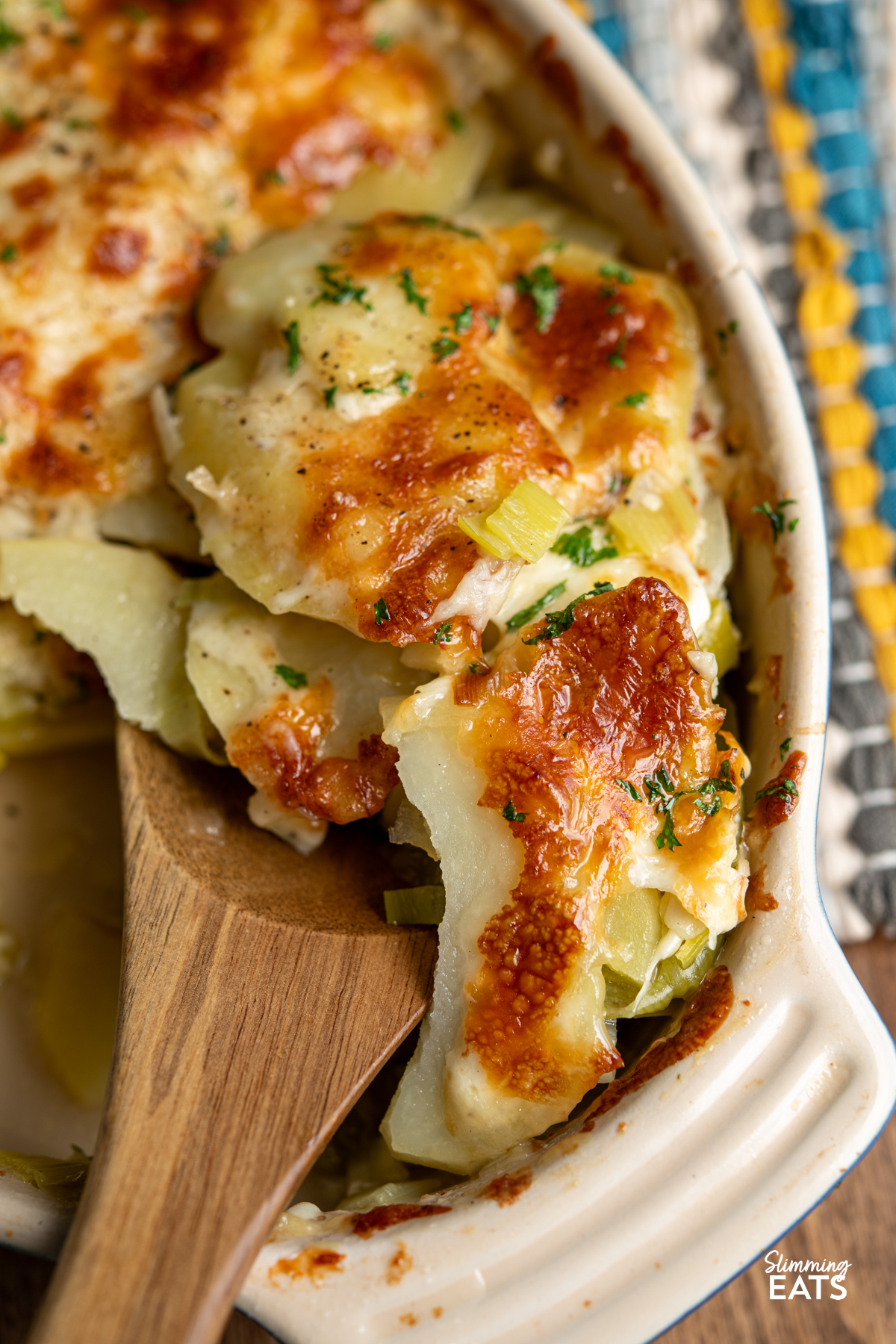 wooden spoon dishing up leek and potato bake from oval baking dish