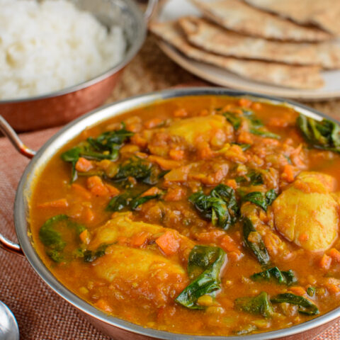 chicken and spinach curry in a dish with rice and bread in background
