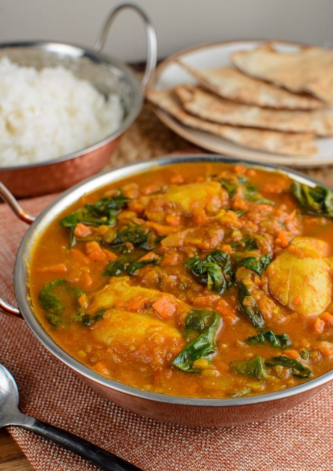 chicken and spinach curry in a dish with rice and bread in background