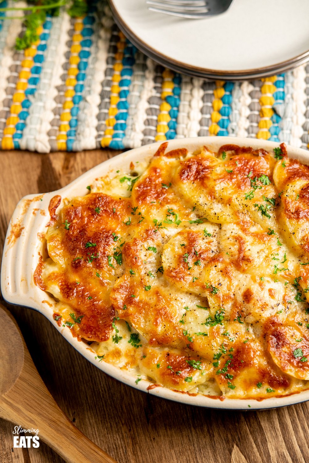 cheesy leek and potato bake in a le Creuset oval dish on wooden board with plates and fork