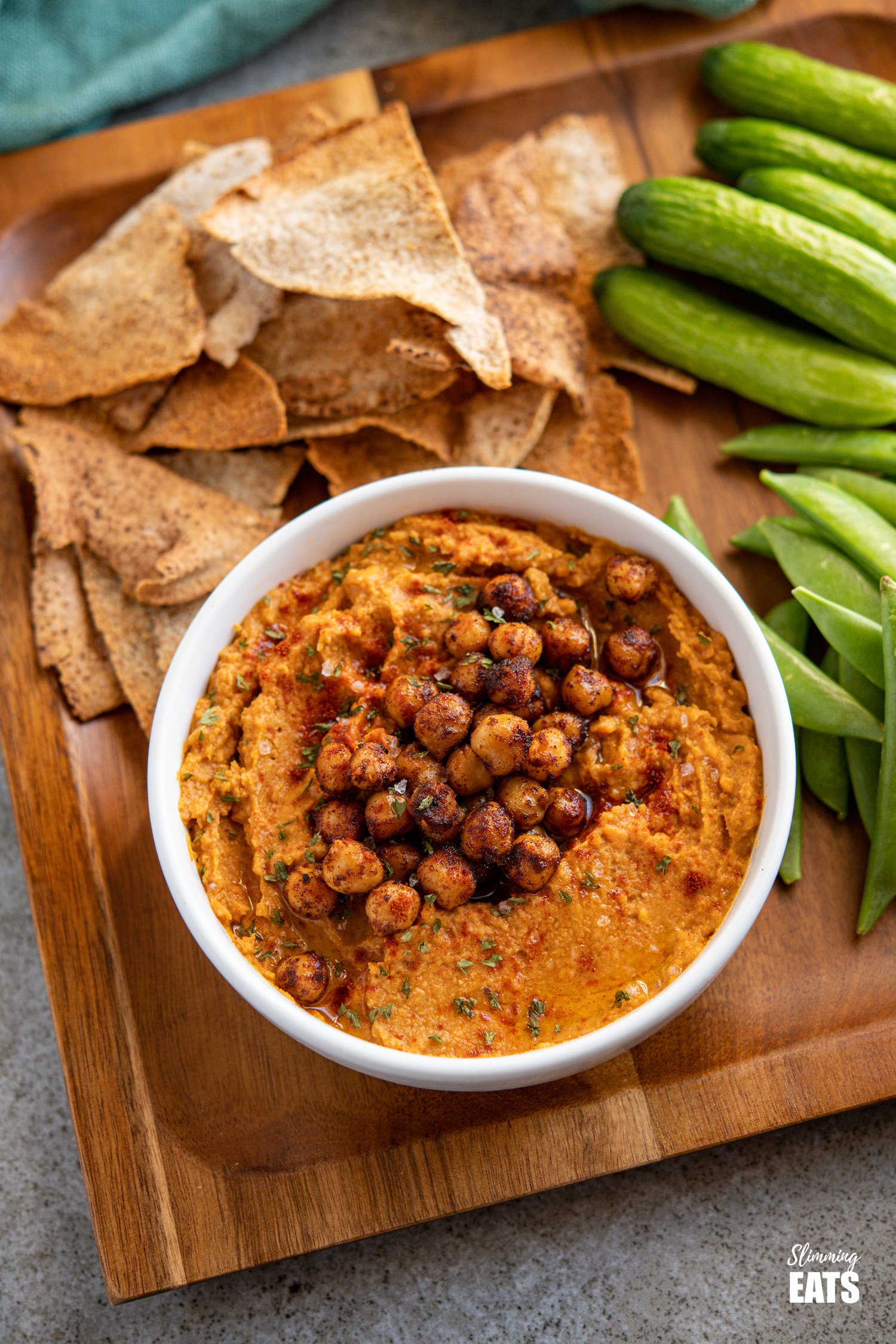 roasted sweet potato hummus topped with toasted chickpeas in a white bowl on wooden tray with pita chips and vegetable crudites