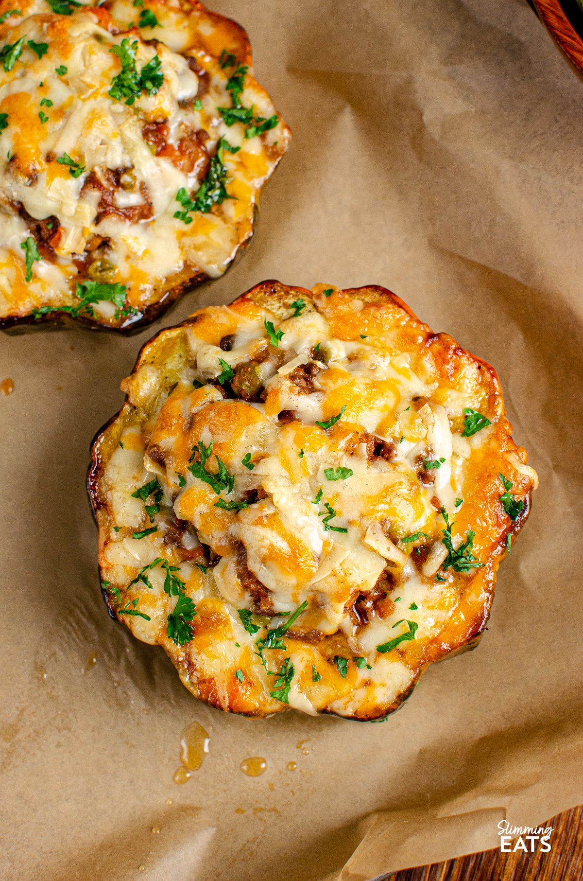 Delicious baked acorn squash stuffed with ground beef and vegetables in seasoned tomato sauce, topped with melted cheese. Calorie Counting, Slimming World and Weight Watchers friendly cheese topped stuffed acorn squash or parchment lined tray