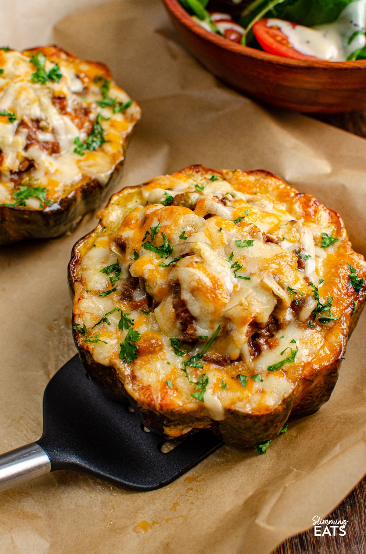 cheese topped stuffed acorn squash half on spatula being lifted from a parchment lined tray 