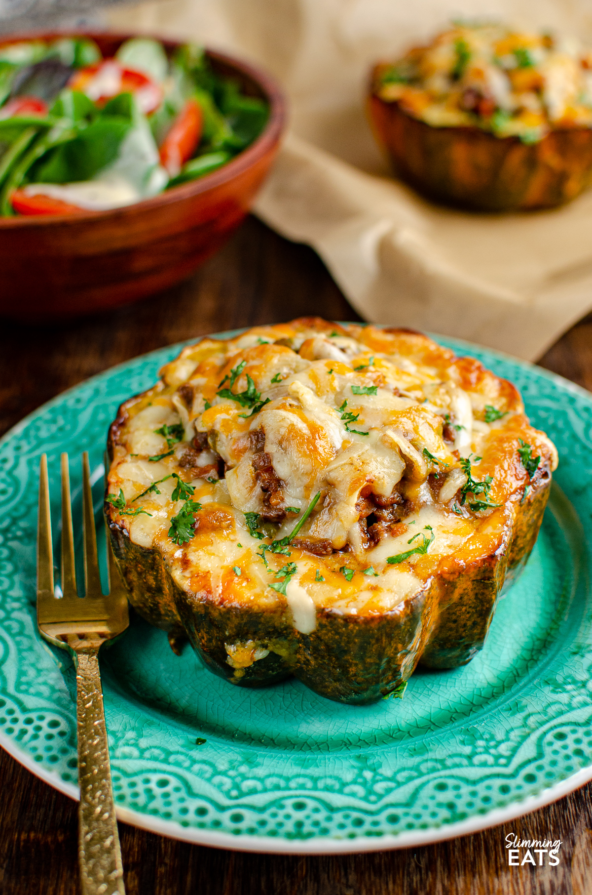 stuffed acorn squash half on teal plate topped with cheese, gold fork placed to left