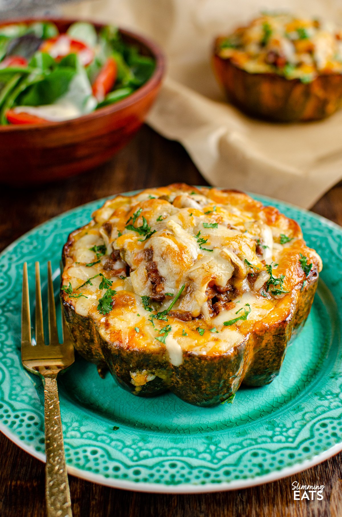 stuffed acorn squash half on teal plate topped with cheese, gold fork placed to left