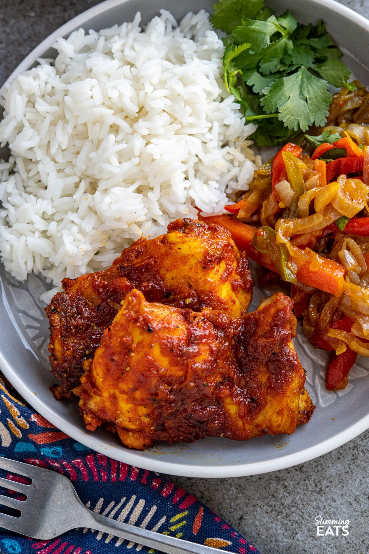Oven Baked Chicken Thighs marinated in a delicious Fusion style sauce over a bed of vegetables. An easy any night of the week recipe that the whole family will love. Gluten Free, dairy free, Slimming World and Weight Watchers friendly close up of oven baked fusion chicken thighs on grey white rimmed plate with baked vegetables rice