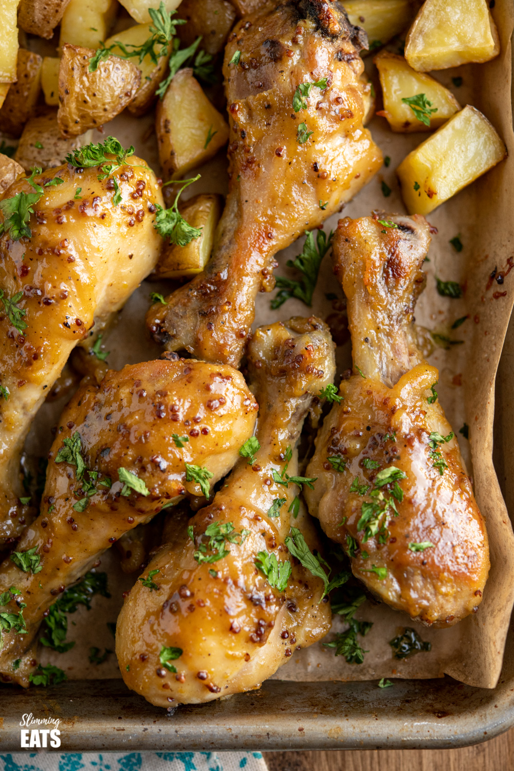 honey mustard chicken drumsticks with potatoes on a tray lined with parchment