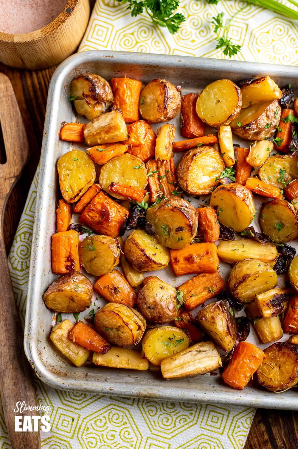 Healthy Delicious Rosemary Roasted Potatoes, Parsnips, Carrots and Onion the perfect addition to any main meal. Gluten Free, Dairy Free, Vegan, Slimming Eats and Weight Watchers friendly Rosemary Roasted Potatoes, Parsnips, Carrots and Onion on baking tray on wooden board with green pattern tea towel