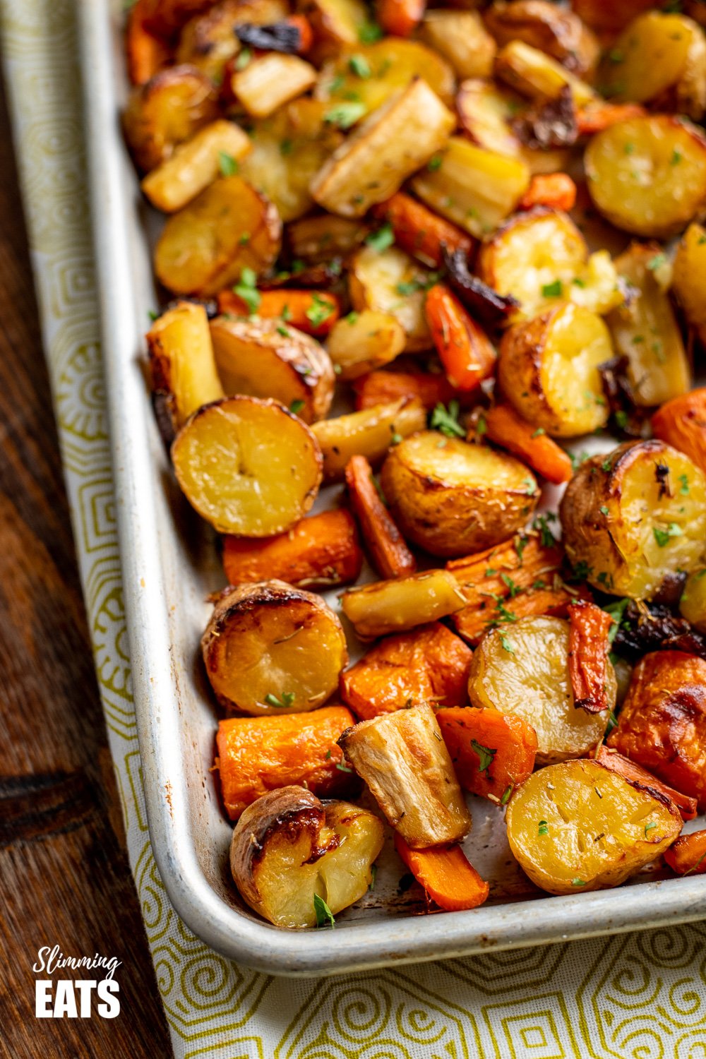 close up of Rosemary Roasted Potatoes, Parsnips, Carrots and Onion on baking tray sprinkled with fresh parsley