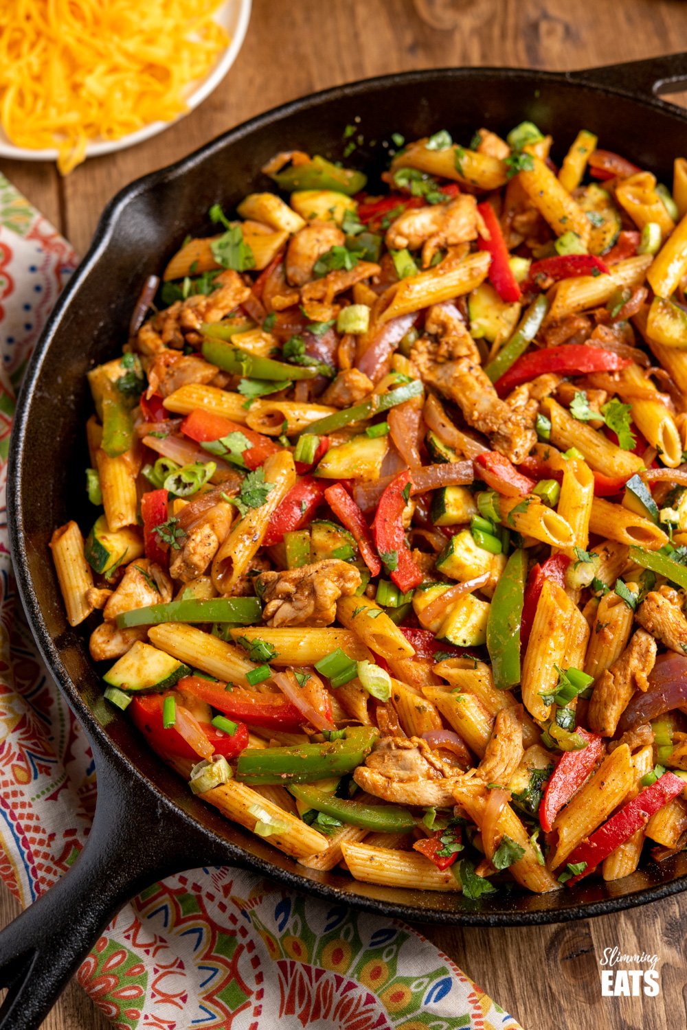 close up of Fajita Chicken Pasta in a lodge cast iron skillet with cheddar in white bowl