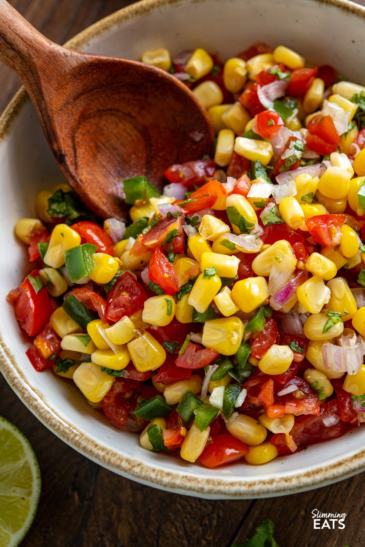 Easy Corn and Tomato Salsa - this quick and easy fresh salsa is the perfect side for barbecues, grilled proteins and more.Gluten free, dairy free, vegetarian (vegan), Slimming World and Weight Watchers friendly close up of Easy Corn and Tomato Salsa in white bowl with light brown rim and wooden spoon