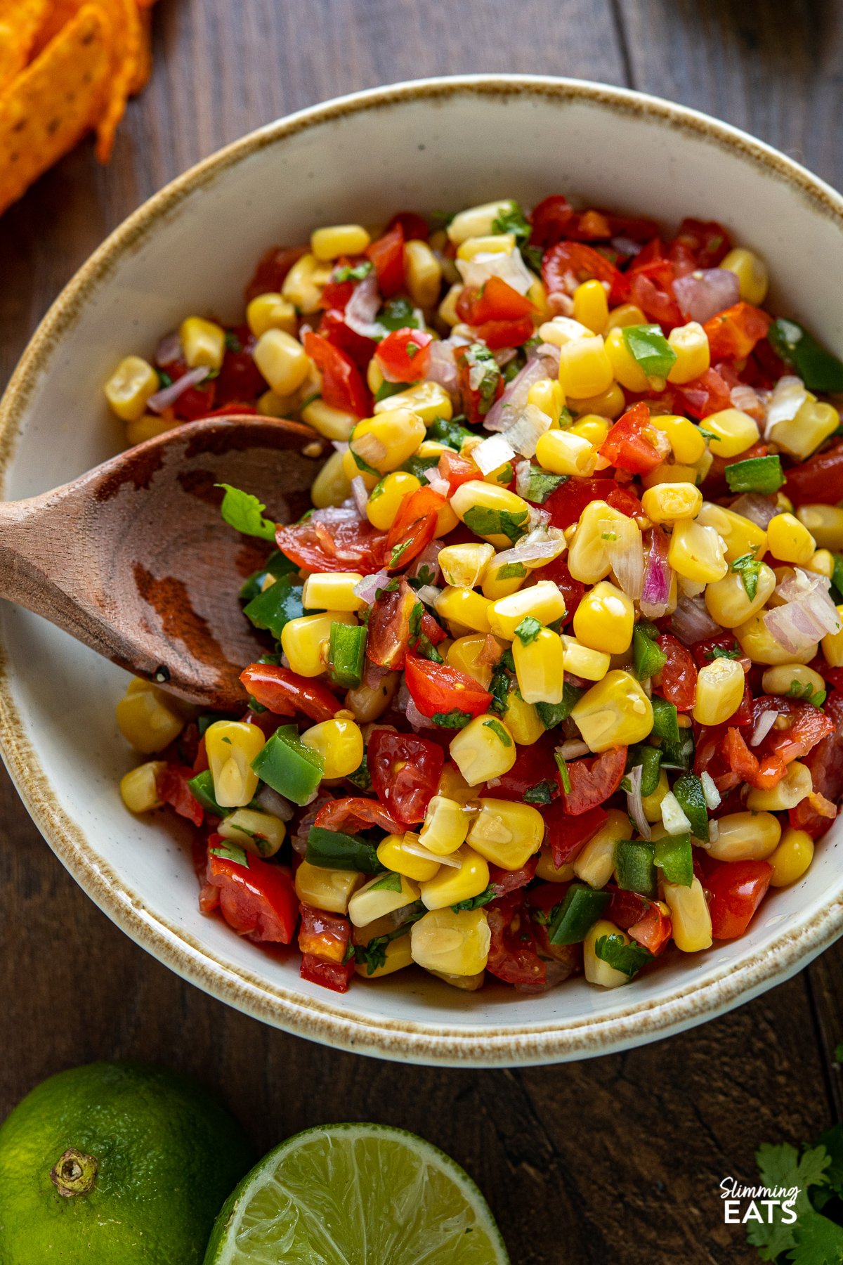 Easy Corn and Tomato Salsa - this quick and easy fresh salsa is the perfect side for barbecues, grilled proteins and more.Gluten free, dairy free, vegetarian (vegan), Slimming World and Weight Watchers friendly close up of Easy Corn and Tomato Salsa in white bowl with light brown rim and wooden spoon
