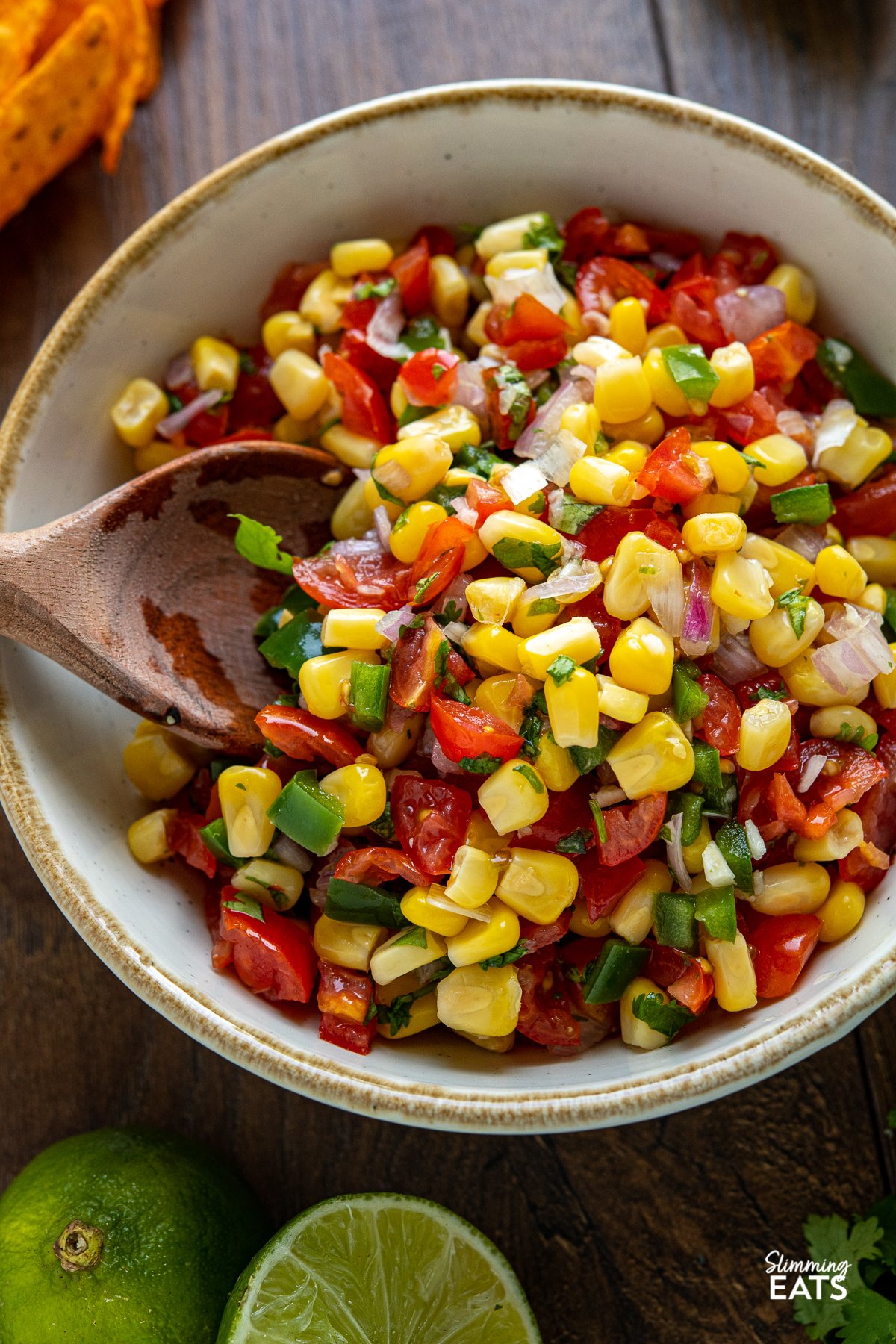 close up of Easy Corn and Tomato Salsa in white bowl with light brown rim and wooden spoon