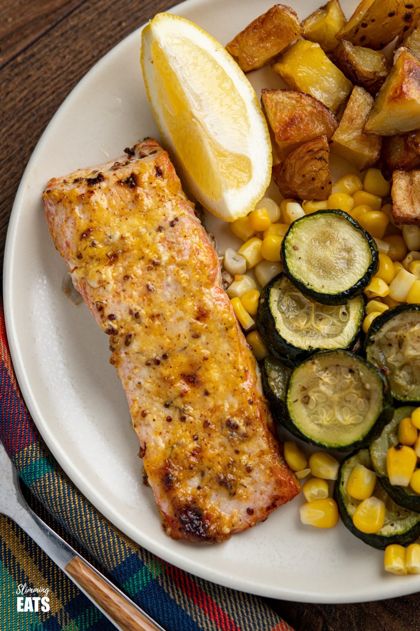 Oven Baked Mustard Salmon Fillets on white plate with roast potato cubes, zucchini and lemon wedge