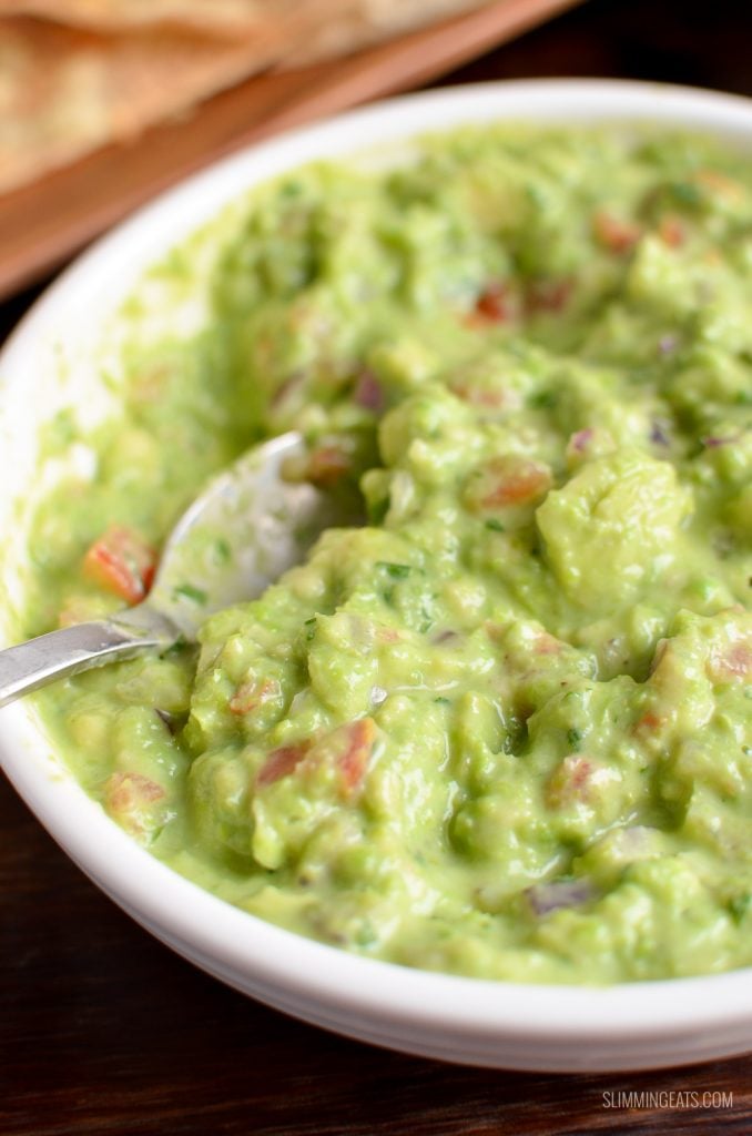 close up of spoon dipped in pea guacamole in white dish