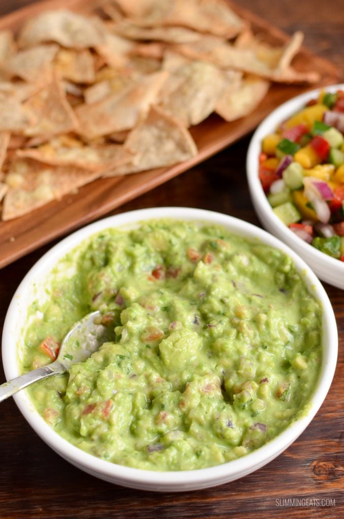 pea guacamole in white dish with spoon and pita chips and mango salsa in background