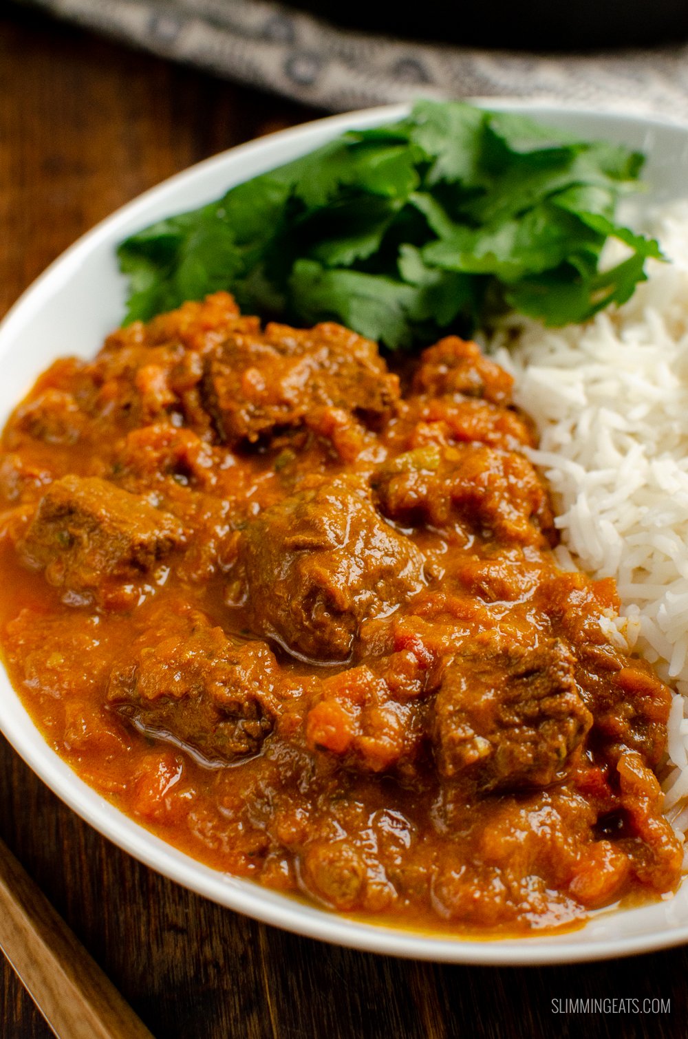 close up of Bombay beef curry in white bowl with rice and coriander.