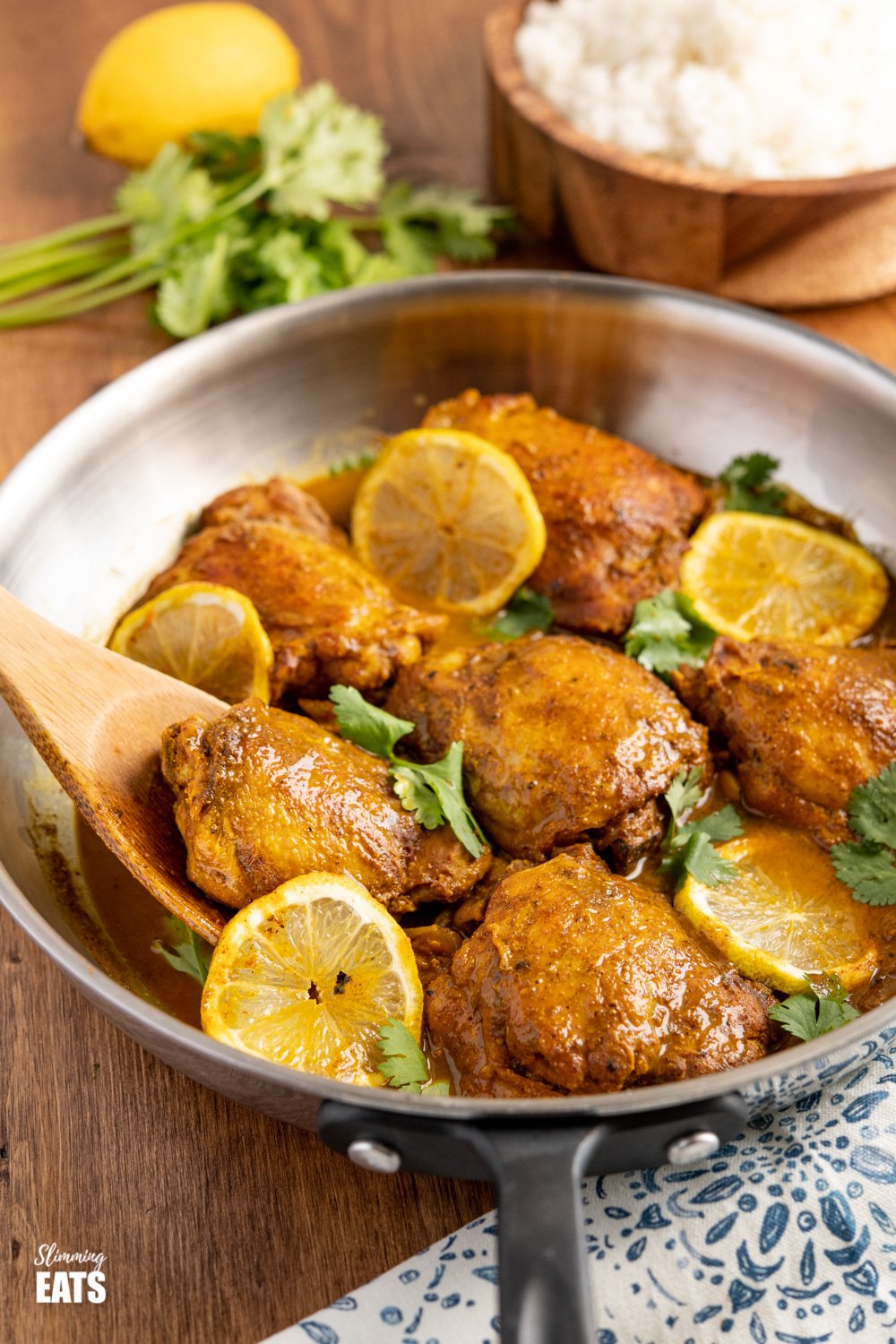 lemon chilli chicken in stainless steel skillet on wooden table with bowl of rice in background