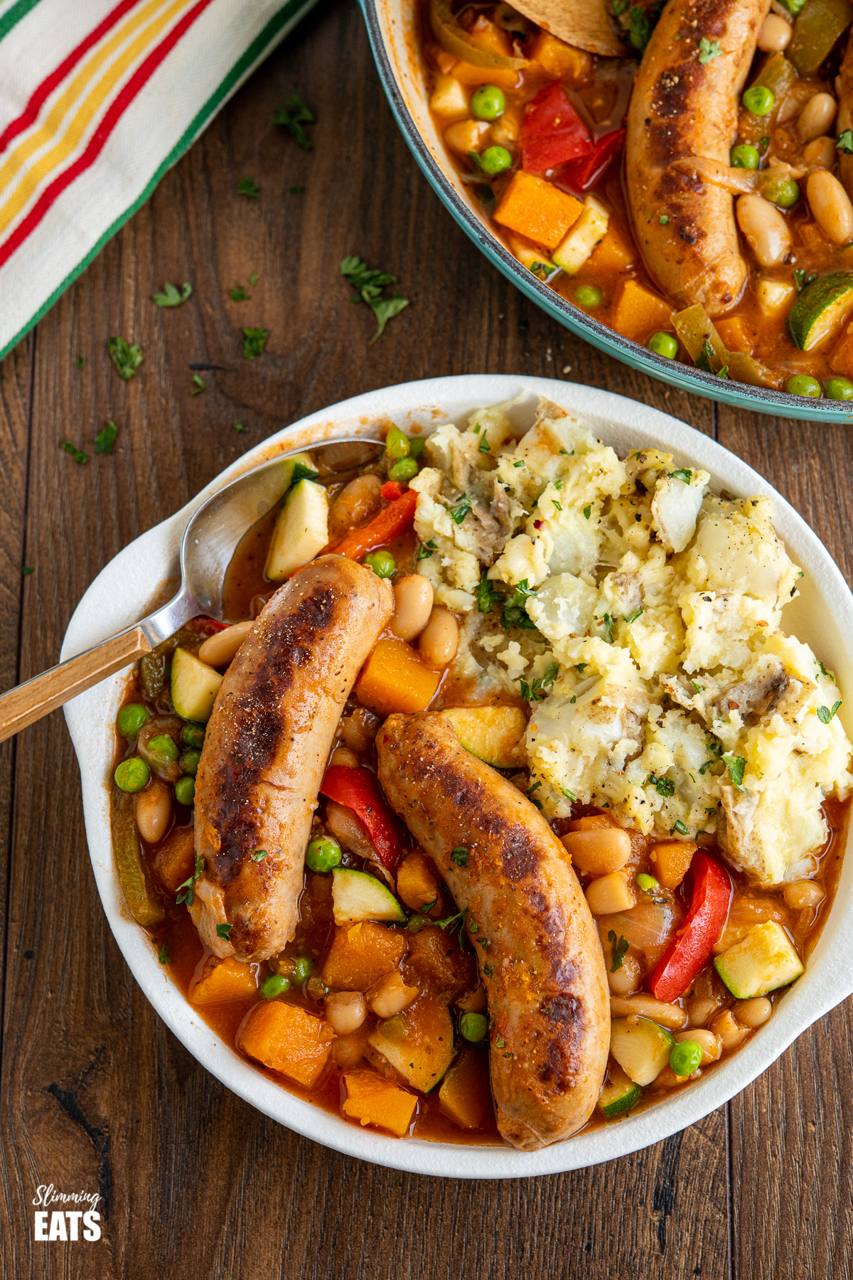 Delicious Sausage Casserole in white bowl with mashed potatoes and wooden handle spoon 