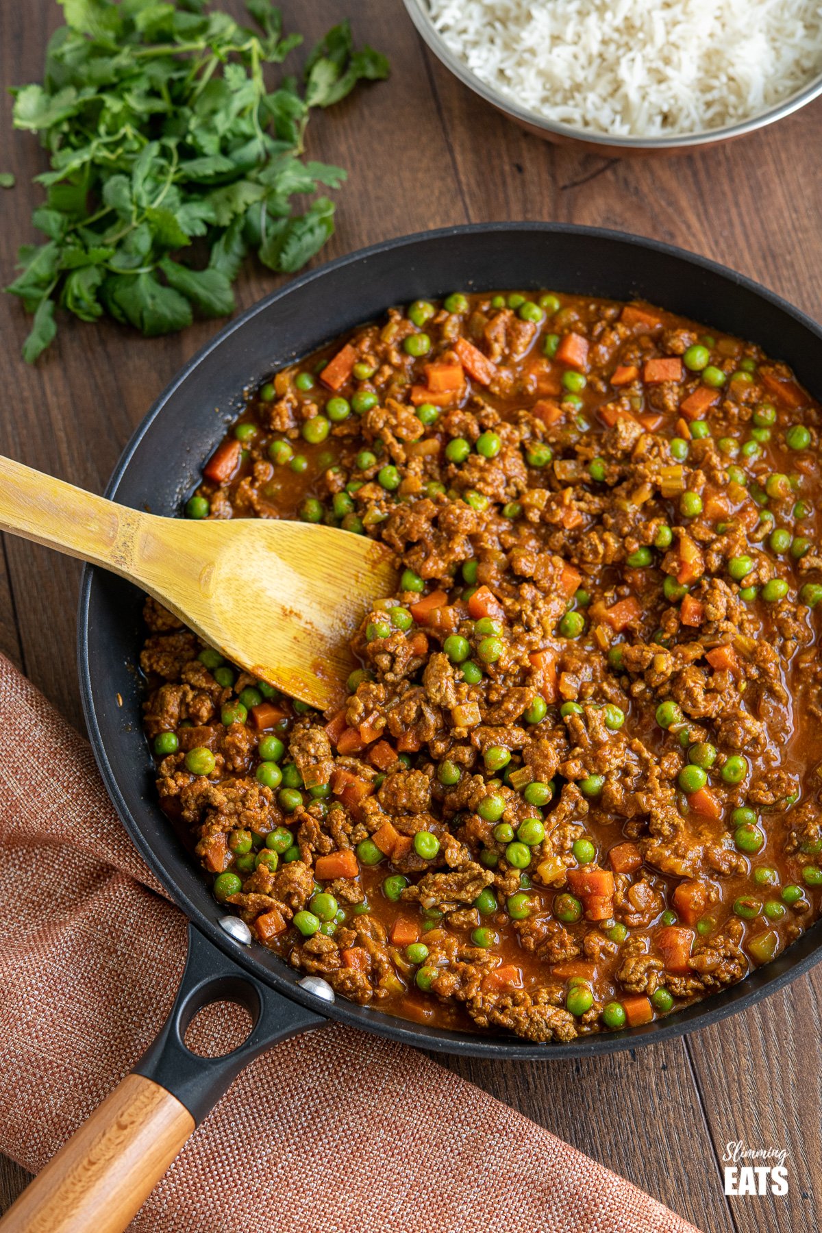 Easy Keema Curry in black frying pan with wooden handle and bowl of rice and coriander in background