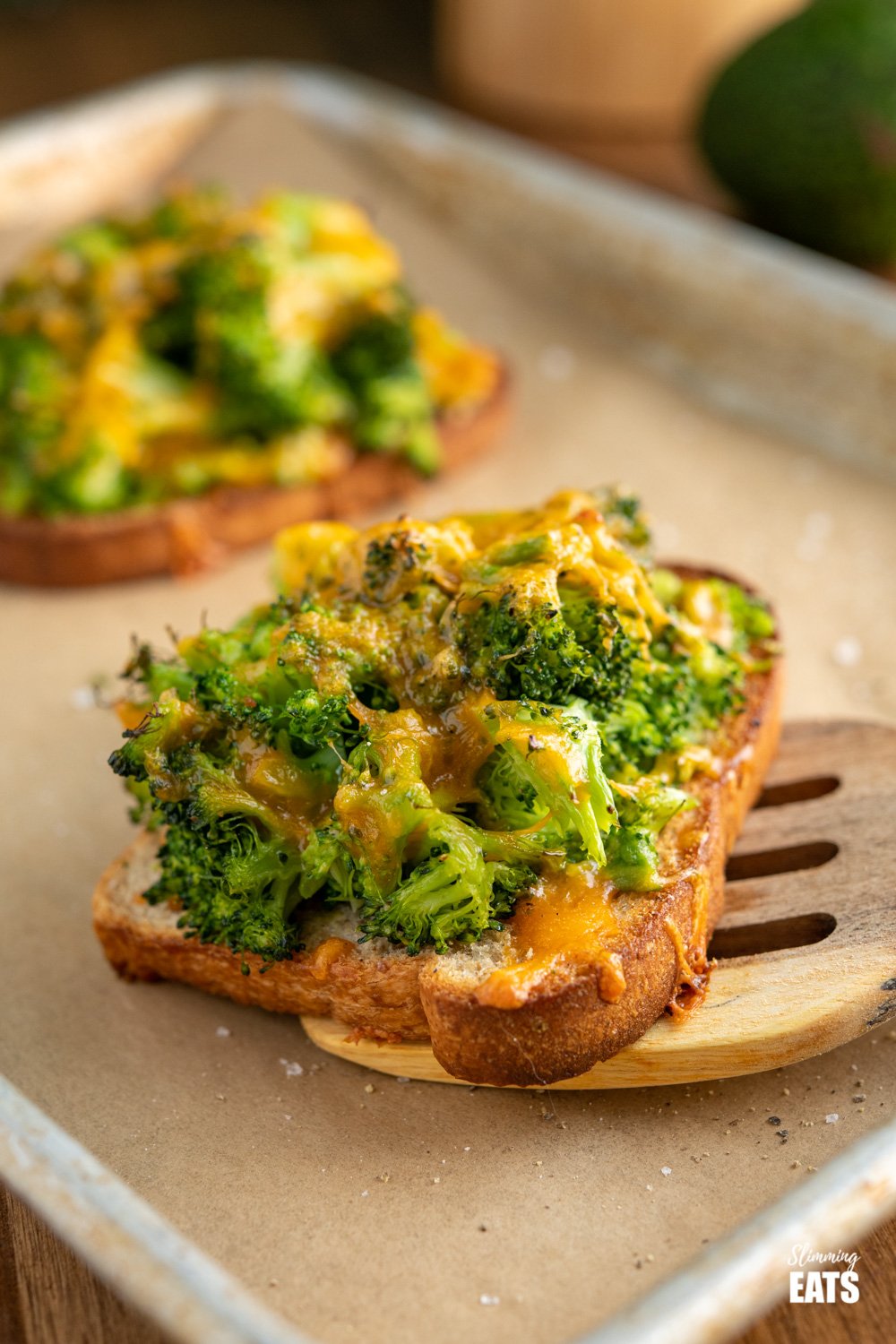 Cheesy Broccoli Avocado Toasts - crispy oven baked toast, topped with cheesy broccoli goodness for a perfect any time of day combo. #broccoli #avocado #slimmingeats #weightwatchers #cheddar cheesy broccoli avocado toasts on parchment lined baking tray