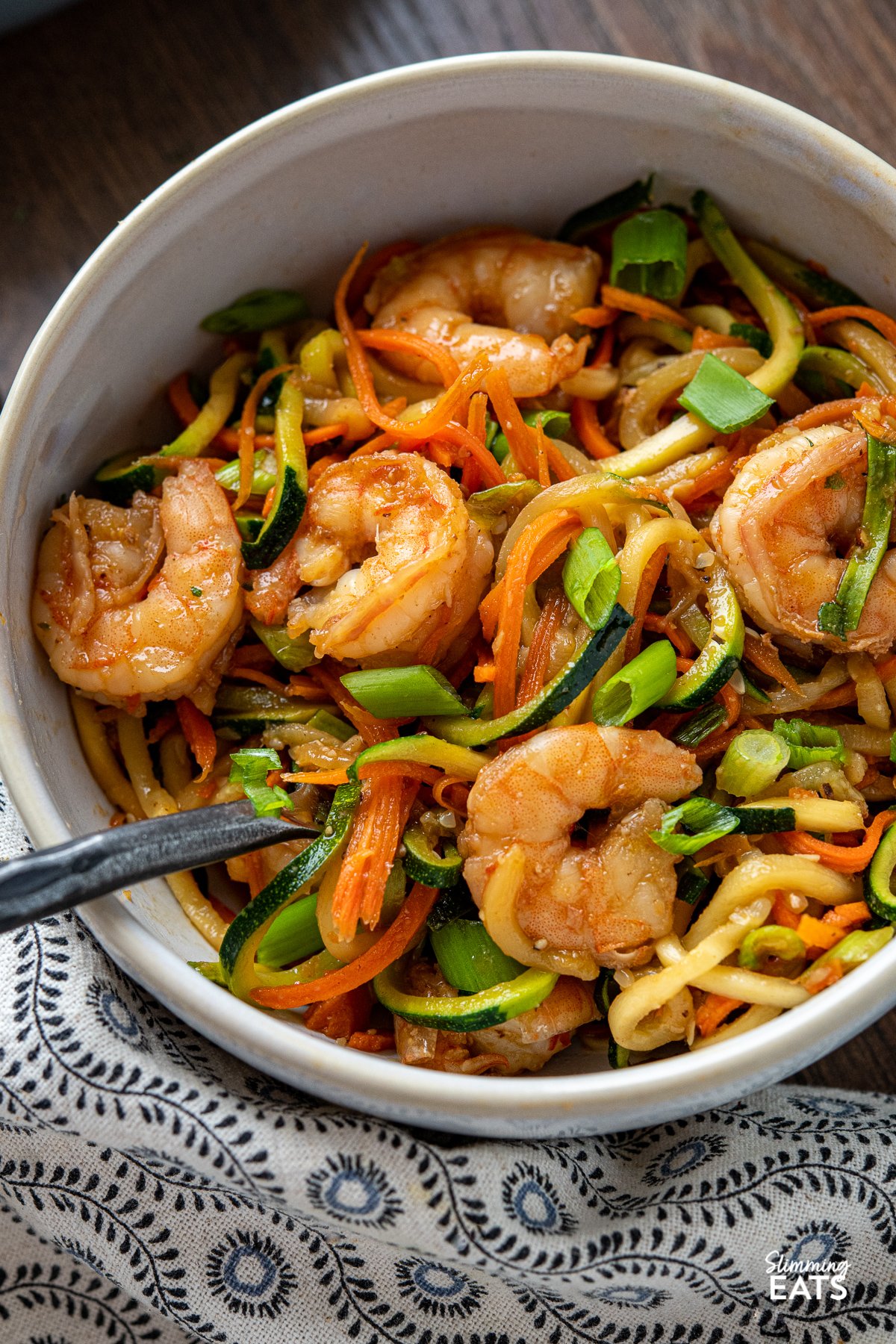 Quick Sweet Chilli Prawns with Vegetable Noodles - a quick and easy stir fry recipe that is lighter on the carbs with some healthy spiralized vegetable noodles. Slimming World and Weight Watchers friendly close up Quick Sweet Chilli Prawns with Vegetable Noodles in a white bowl with fork