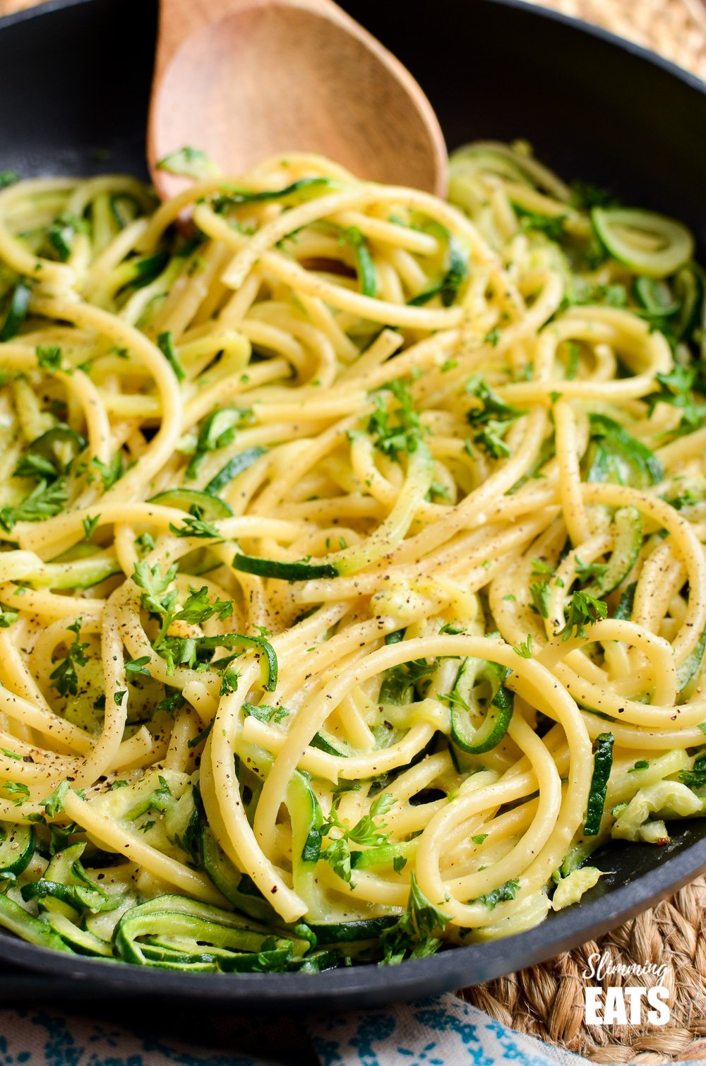 Delicious Syn Free Courgette and Parmesan Pasta - a simple quick pasta recipe with spiralized courgette. Vegetarian, Slimming World and Weight Watchers friendly close up of courgette and parmesan pasta in black frying pan with wooden spoon.