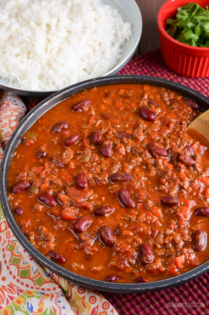 Chilli Con Carne in black frying an with bowl of rice and small red bowl with cilantro